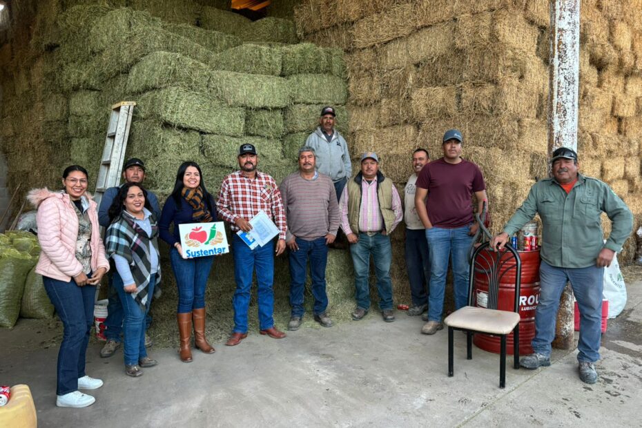Group photo of people standing in front of a large stack of hay bales. One of them is holding a Sustentar poster.